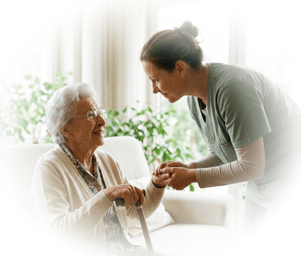 Junge Betreuungskraft reicht einer sitzenden Seniorin liebevoll die Hand