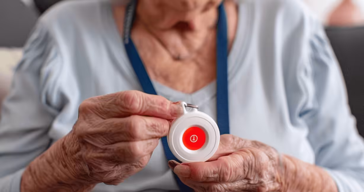 Eine ältere Frau hält ein Notrufgerät mit einem roten Licht und konzentriert sich darauf.